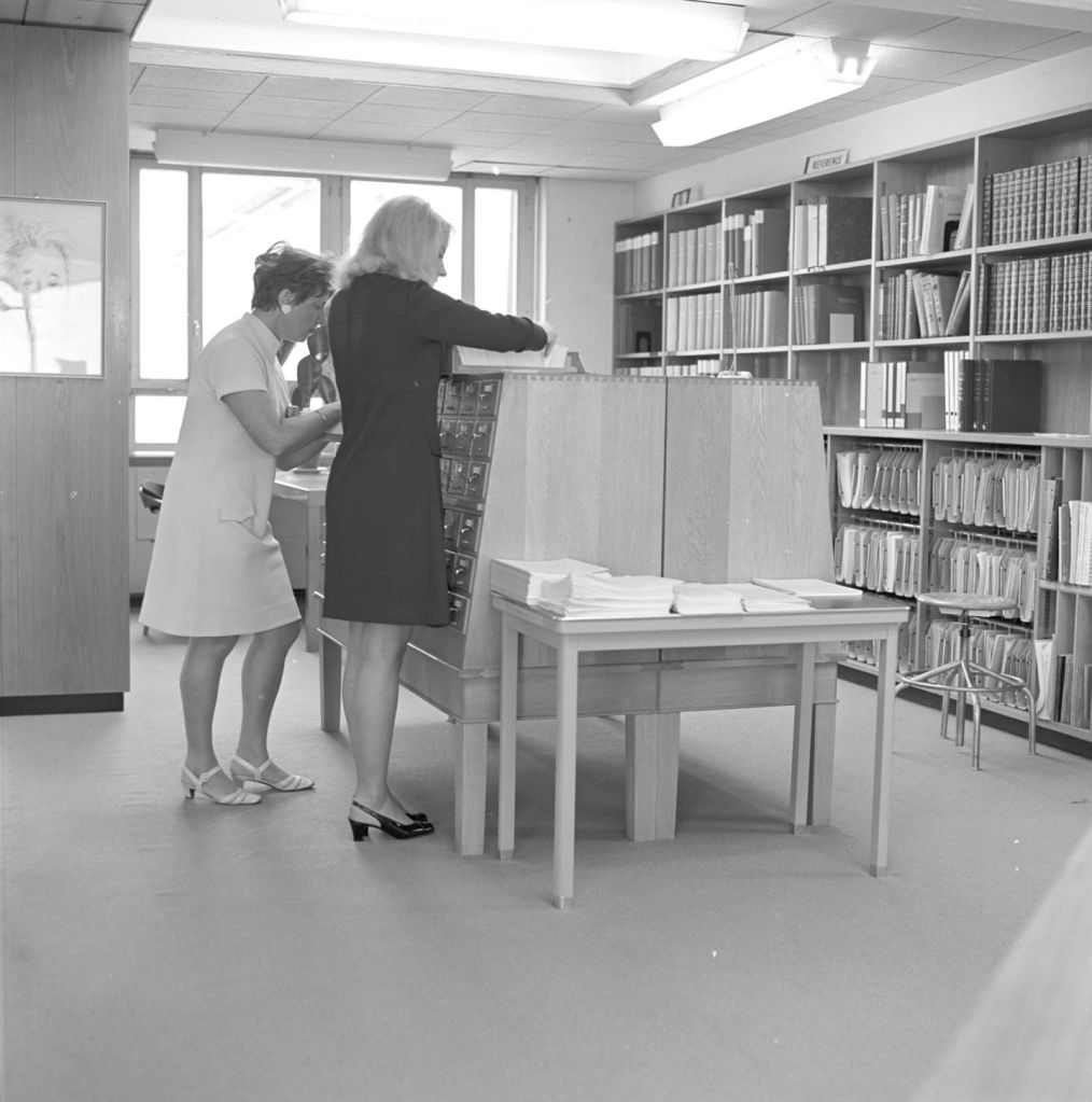 Two female library staff sorting papers on top of the card catalog at the CERN Central Library.